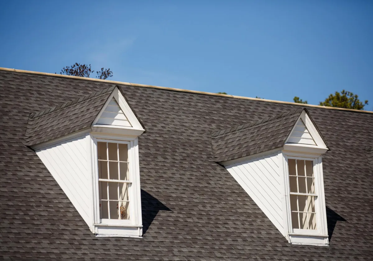 Two white wood dormers on a grey shingle roof under blue sky
